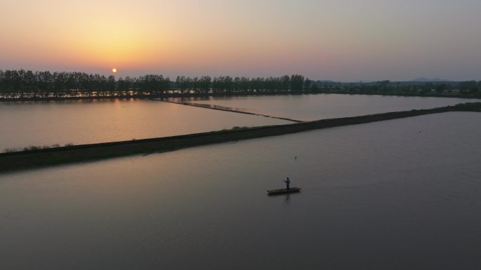 夕阳下渔村的鱼塘里渔民正划着小船风景航拍