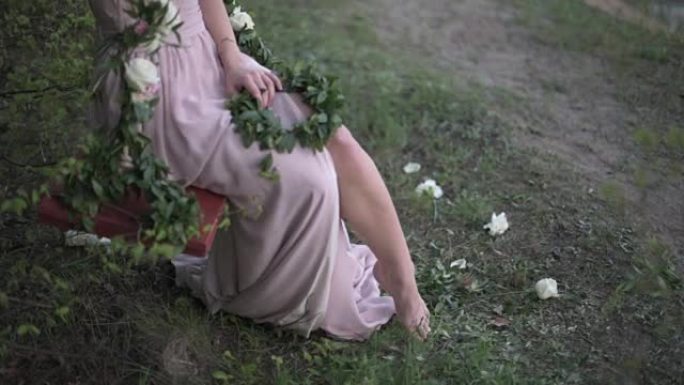 年轻女子穿着轻盈的pinc束腰外衣，嬉戏地露出她的腿，坐在装饰着鲜花的秋千上