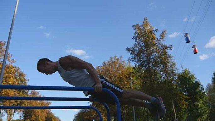 运动男子在城市公园运动场的双杠上俯卧撑。强壮的年轻肌肉发达的家伙在夏天户外训练。运动员在操场上锻炼。