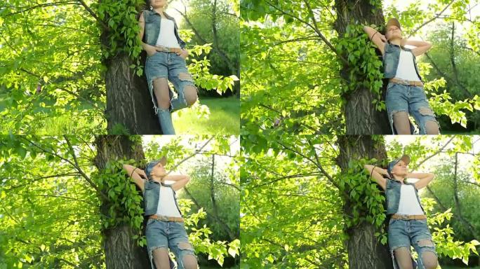 日落时分，穿着牛仔裤衣服的漂亮女孩在森林里的树上摆姿势。