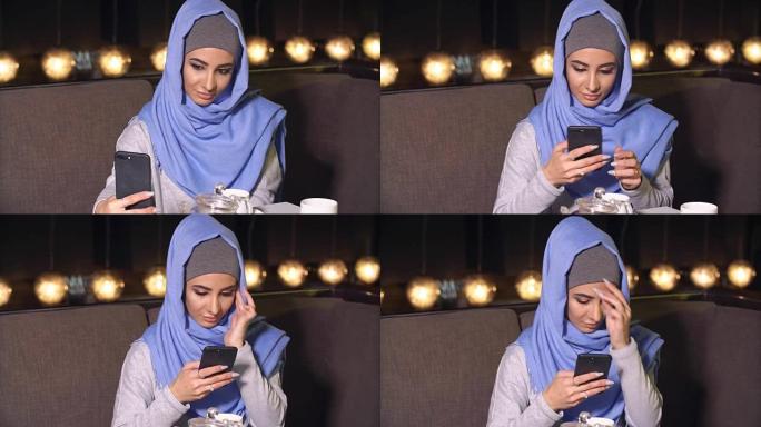 美丽的穆斯林女孩在咖啡馆使用智能手机。现代穆斯林妇女与新技术