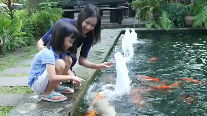 亚洲女孩和母亲在池塘里为鲤鱼喂食食物
