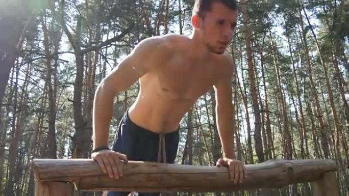 运动员在森林里做俯卧撑。夏天，强壮的年轻肌肉发达的家伙在树林户外训练。运动员在美丽的大自然中锻炼。锻
