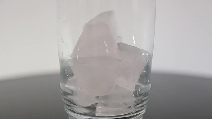 落在白色背景中隔离的透明玻璃中的冰块
