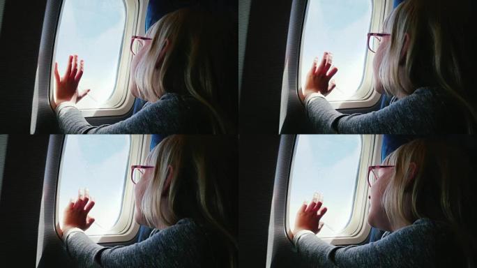 一个戴着眼镜的6岁女孩坐在飞机上，看着窗外。她的手被压在舷窗上-快乐的旅程