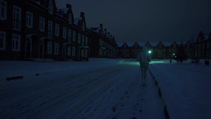 穿着银色夹克的孤独年轻女子晚上在居民区的雪地上行走