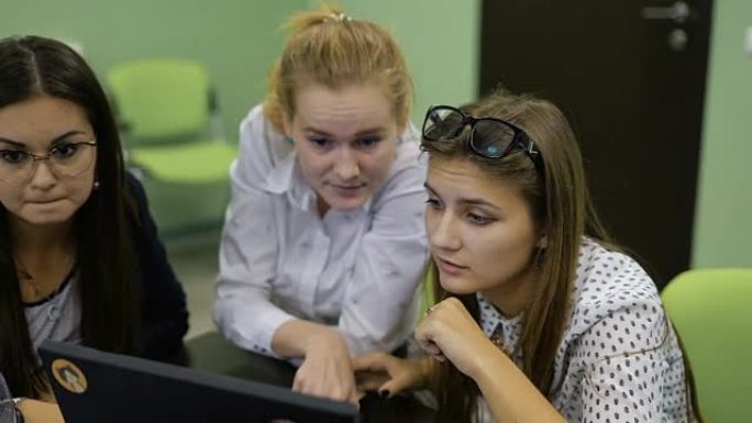 年轻的男女学生坐在办公桌前，与PC一起工作，看着显示器，讨论并准备为观众介绍他们的启动项目。三个年轻