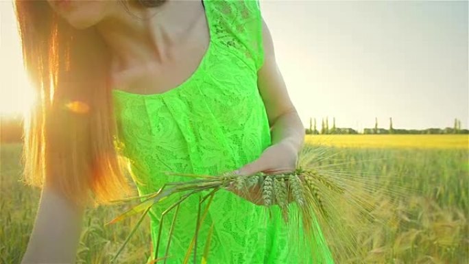 穿着绿色连衣裙的幸福女人在田间编织麦穗花环特写