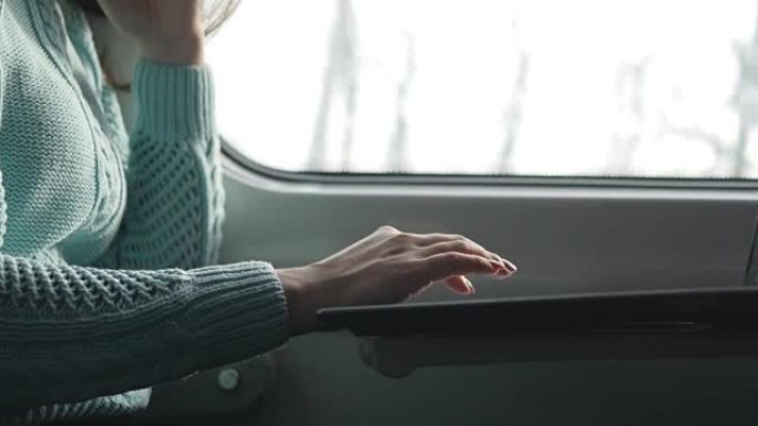 年轻女孩乘火车旅行，使用笔记本。使用笔记本电脑触摸板的女性手。和朋友聊天的女孩。特写