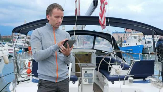 英俊的年轻人站在他的游艇附近。他检查平板电脑上的消息，并在社交网络中结识朋友