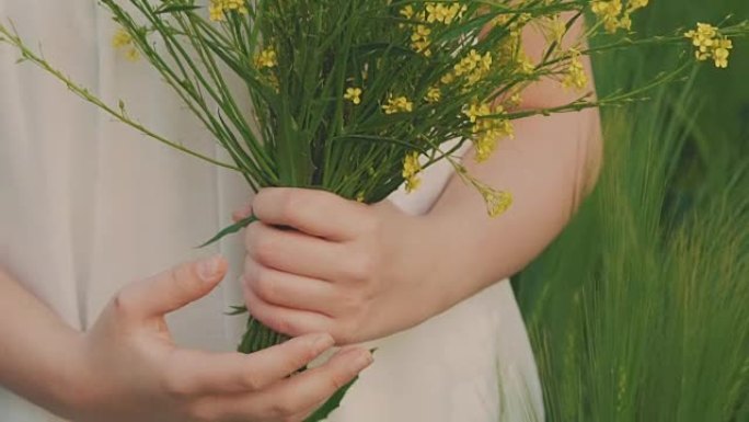 可爱的年轻女孩拿着一束油菜花，在田野里嗅它