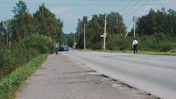 男人竖起大拇指走在乡下的路上。搭便车。汽车。阳光明媚