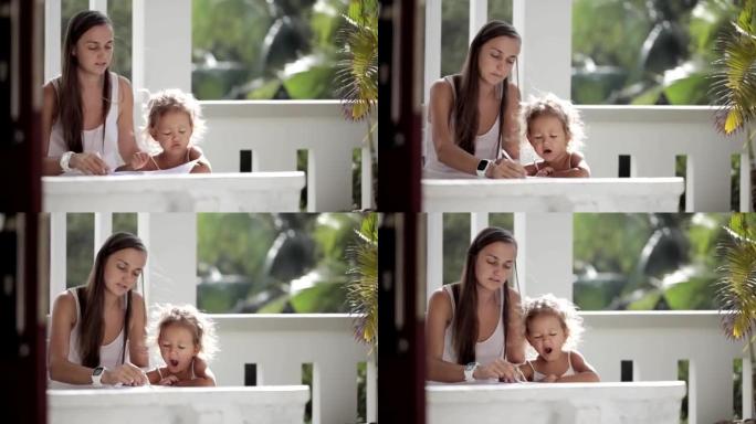 年轻的母亲带着女儿在阳台上画画，背景是棕榈树