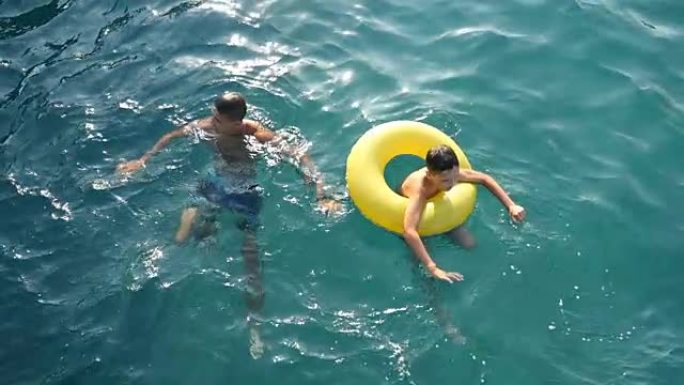 年轻人和一个穿着充气环的男孩在slo-mo的蓝色海水中游泳