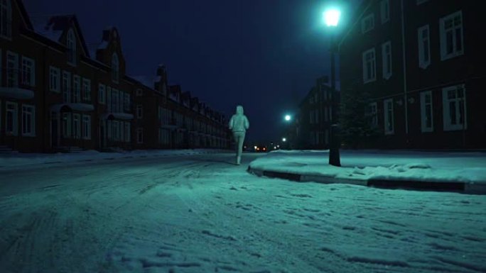 穿着银色冬季夹克的孤独女孩晚上在居民区的雪地上行走