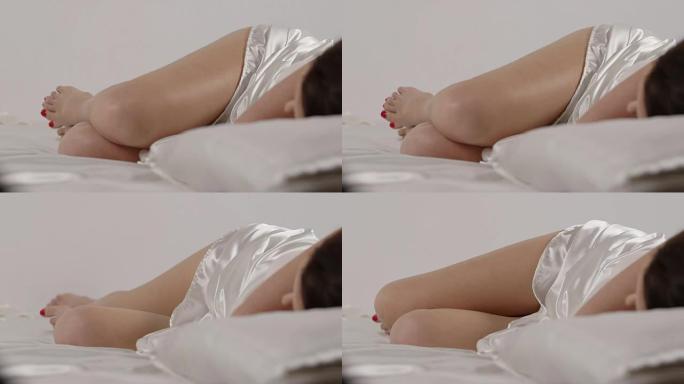 年轻女子躺在床上的白色亚麻布上，以胎儿的姿势睡觉