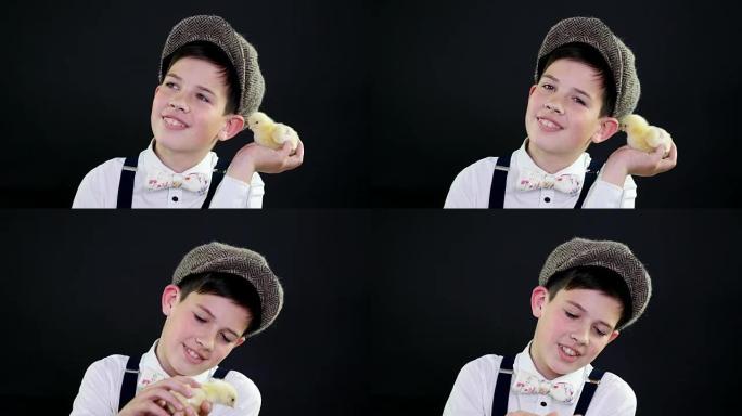 肖像，一个戴着帽子和吊带的漂亮男孩和一只黄色小鸭子玩耍。带有主题装饰的工作室视频