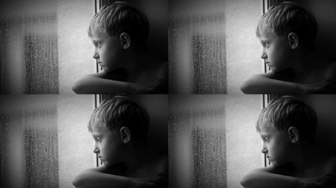 孤独的小男孩透过窗户玻璃看着雨滴