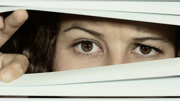 可疑的年轻女子稍微打开百叶窗，然后仔细地环顾四周，可疑而紧张。