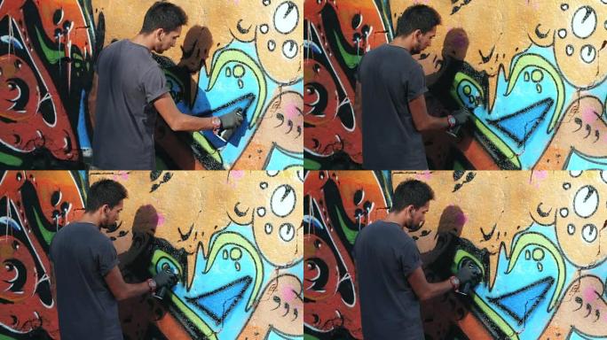 涂鸦艺术家用气溶胶作画。拿着喷雾器的人。缓慢的运动。年轻的城市画家在夏日的阳光下，在城市的街道墙上画