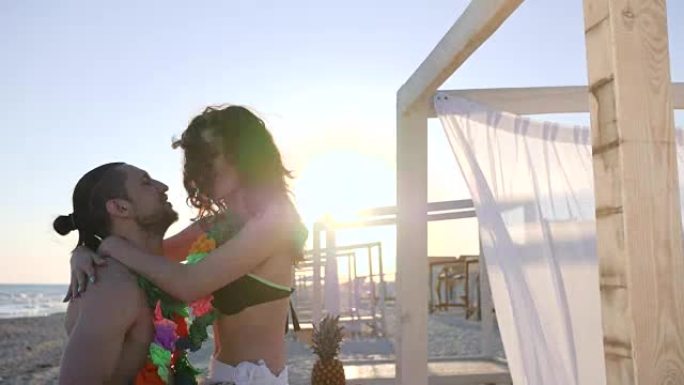 夫妇在夏威夷夏季休息，男人在背光中抱着女人，在海边有五颜六色的花环的朋友，在背景上的年轻人美丽的海滩