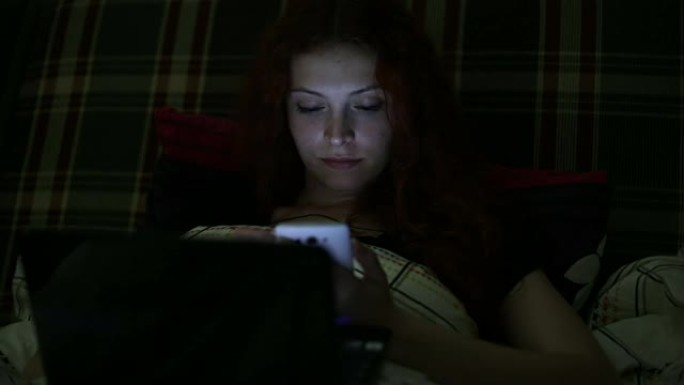 年轻女子带着笔记本电脑晚上躺在家里的床上写短信