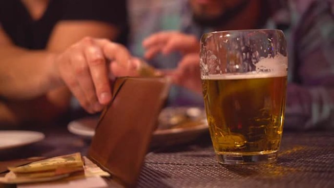 一个年轻人正在dluzyami的酒吧里喝啤酒。淡啤酒泡沫特写。在后台，这家伙有卡佩林。手中的油炸开胃