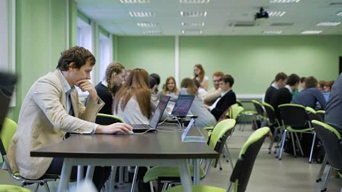 现代大学的教育过程。学生们分组坐在桌旁，用笔记本屏幕学习课程材料。宽敞宽敞的教室