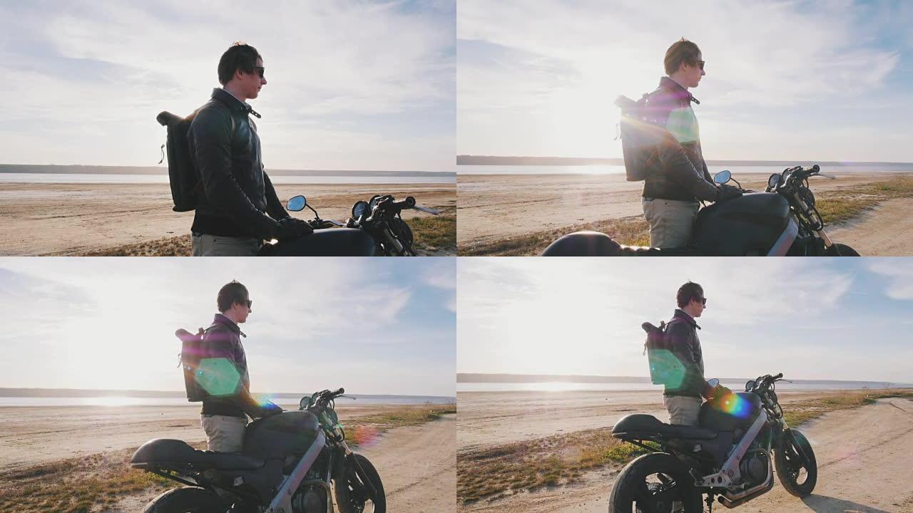 摩托车手在日落时站在沙滩上