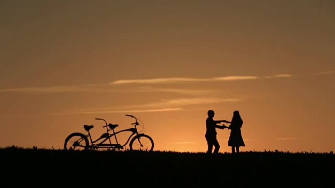美丽的夫妇与双人自行车在神话般的日落背景下的剪影