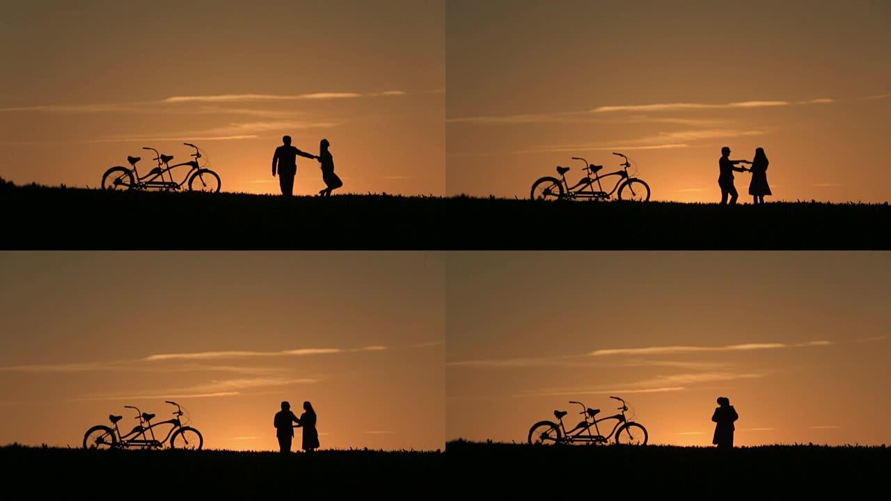 美丽的夫妇与双人自行车在神话般的日落背景下的剪影
