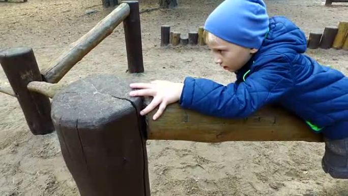 金发小男孩正在做木头。小男孩在操场上玩。