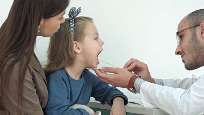 由男医生用压舌板检查喉咙的小女孩