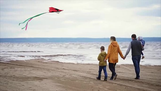幸福的一家人沿着海岸散步。男人，女人，小男孩和女孩在玩