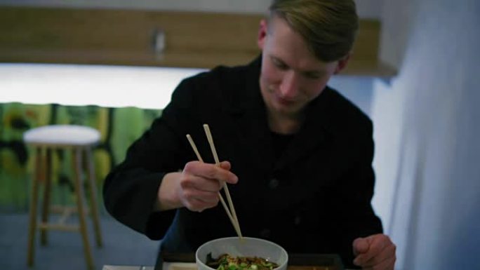 一个男人试图用筷子吃面条的特写镜头。学习如何拿筷子没有成功拿叉子。