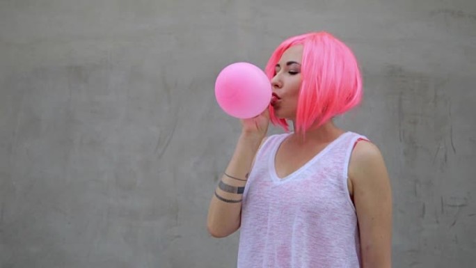 混血时尚潮人少女吹着红色气球戴着粉色假发的特写肖像