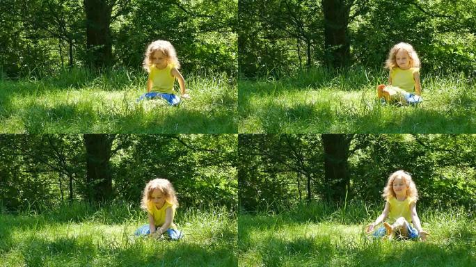 美丽的小女孩的户外肖像，金色的短卷发坐在绿色的草地上，捡起并扔掉。