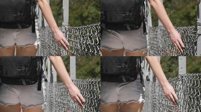 女性手沿着网格表面移动。年轻女子的手臂触摸金属丝围栏。女孩在暑假散步，用手指沿着桥的守卫。关闭慢动作