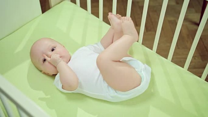 婴儿躺在家里的婴儿床里吃手指