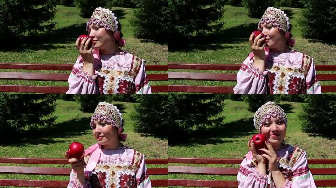 穿着俄罗斯民族服装的女孩嗅着红苹果