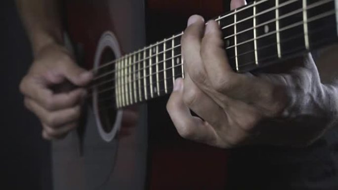 男子在黑色背景上弹奏木吉他，手指慢动作