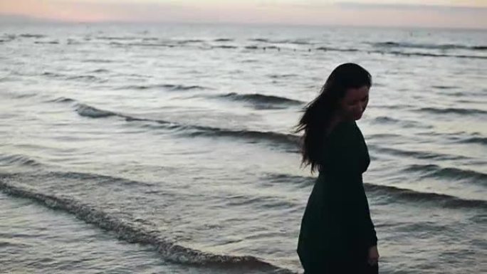 穿着深色连衣裙的女孩在海岸的水上摇头发。拍照。微笑。模。海