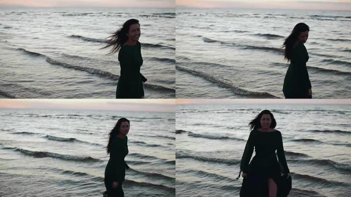 穿着深色连衣裙的女孩在海岸的水上摇头发。拍照。微笑。模。海