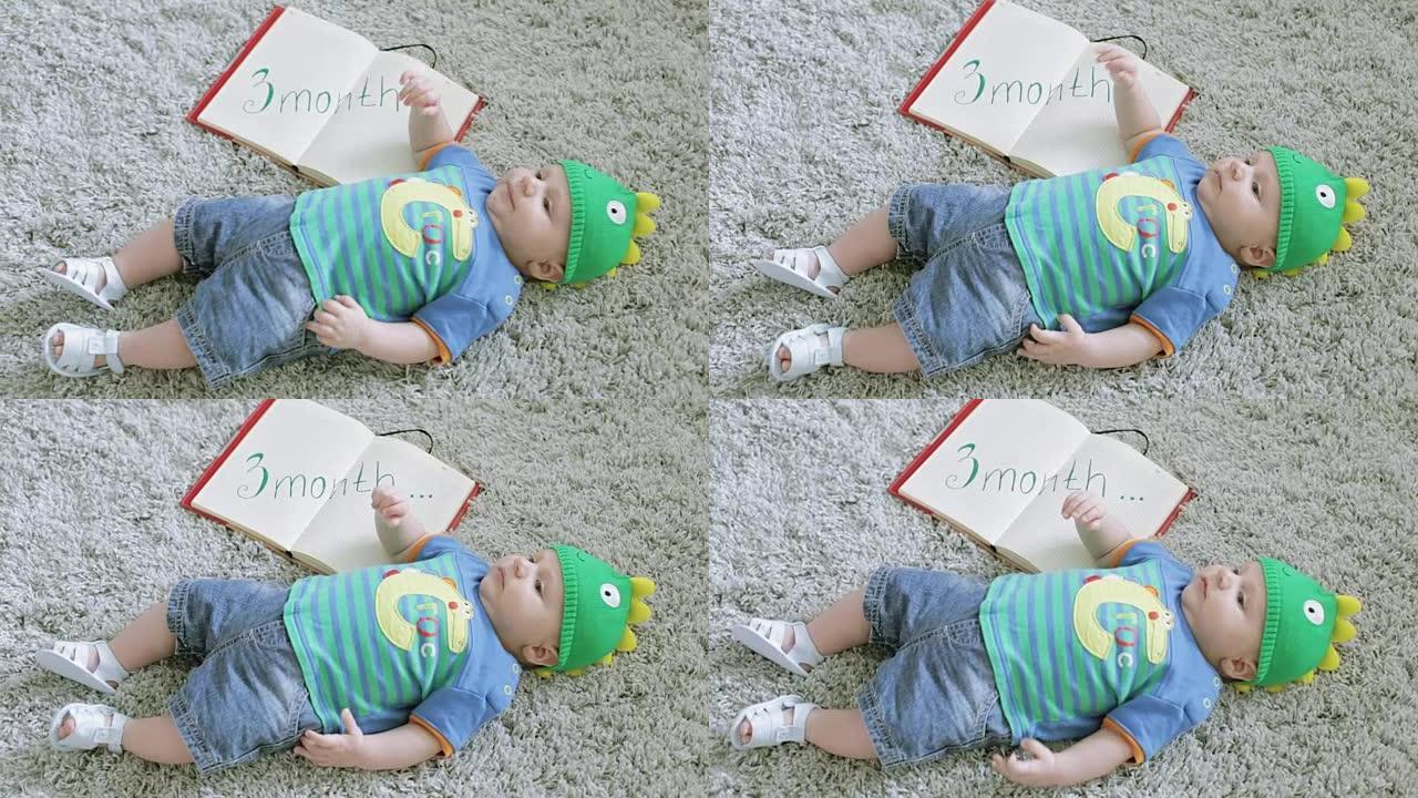 戴着绿龙帽子的三个月婴儿躺在他背上的灰色地毯上。