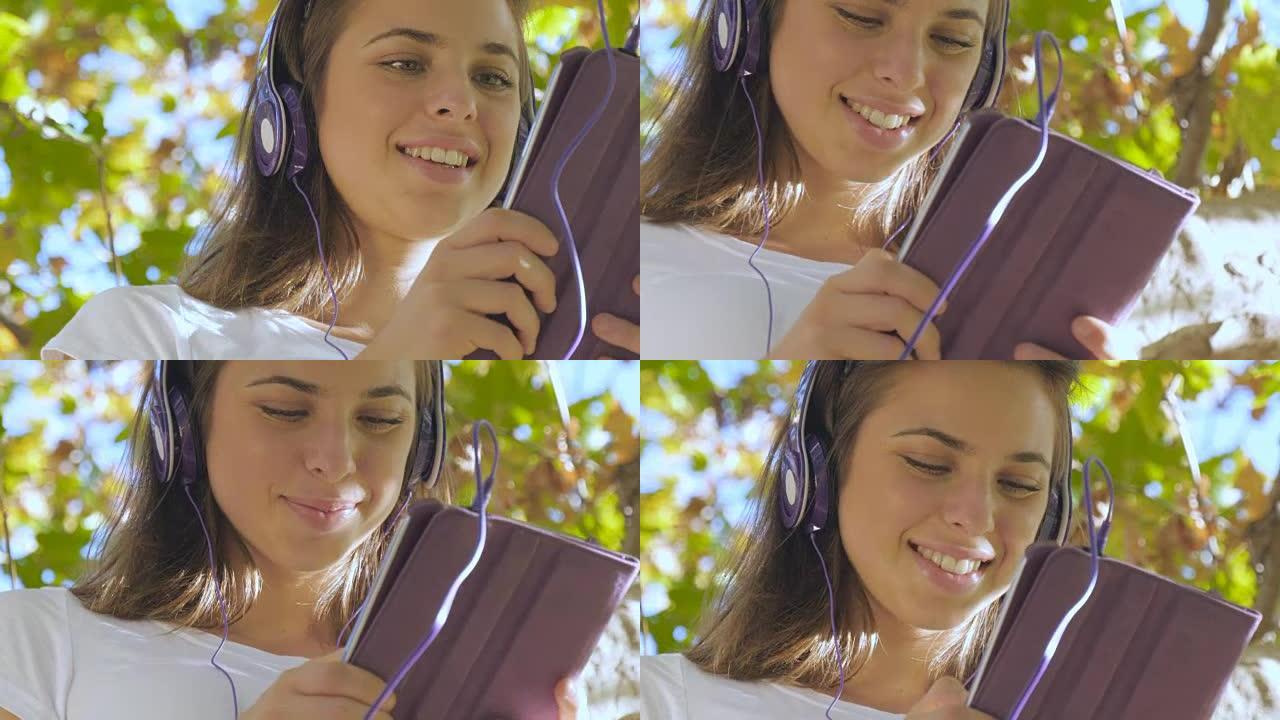 迷人的年轻女子平板电脑用耳机听音乐秋天