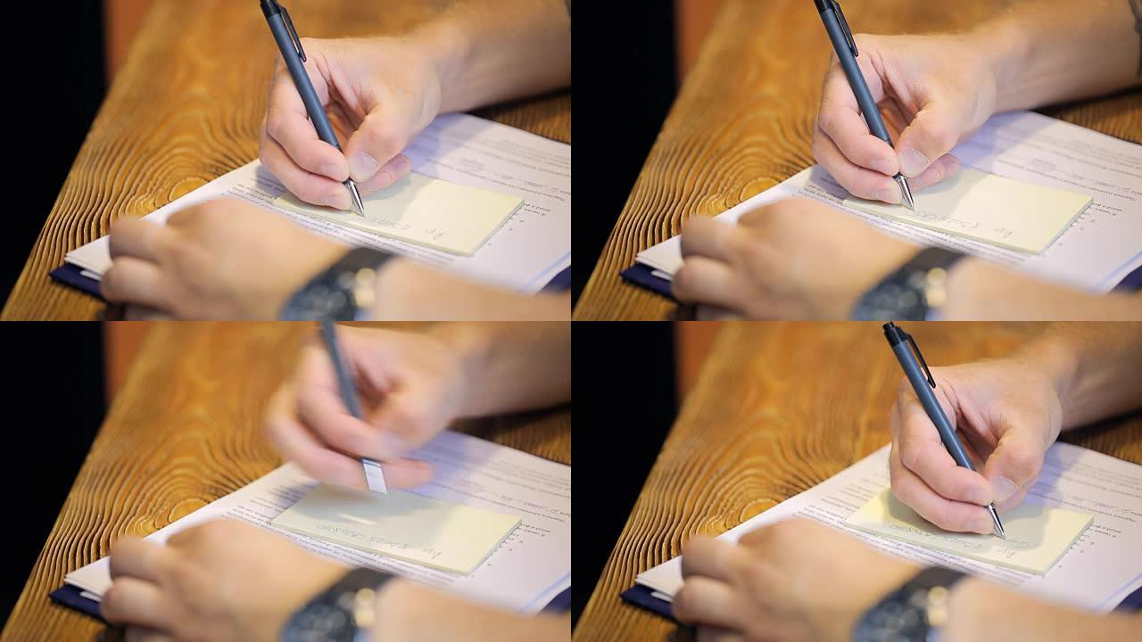 男子坐在木桌旁，用中性笔在贴纸上写短信