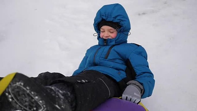 一个快乐的孩子骑在雪山上的雪管中摔倒