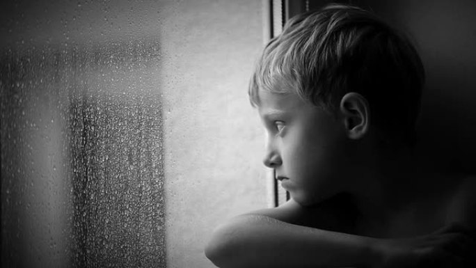 孤独的小男孩透过窗户玻璃看着雨滴