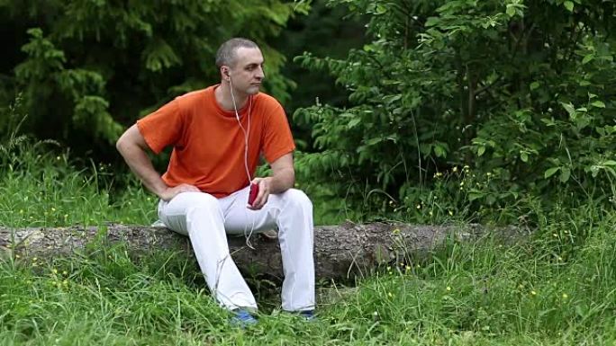 穿着红色智能手机的男人坐在森林里倒下的树上听音乐