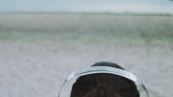 摄像机从戴着耳机的女性头部穿过大海和海滩到达天空